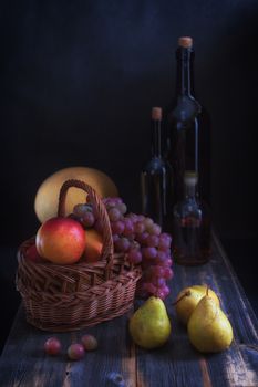 Fruit in a basket, a melon and bottles with wine on old wooden boards