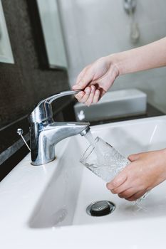 Woman filling a glass of water from a stainless steel or chrome tap or faucet, close up on her hand and the glass with running water and air bubbles.