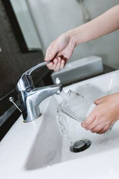 Woman filling a glass of water from a stainless steel or chrome tap or faucet, close up on her hand and the glass with running water and air bubbles.
