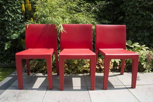 three red plastic chairs in garden with green plants and yellow flowers