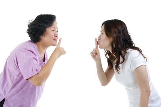 Portrait of Asian adult daughter and her senior mother gesturing quiet sign, finger on lips, isolated on white background.