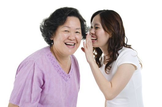 Portrait of Asian adult daughter telling secret to her senior mother, isolated on white background.