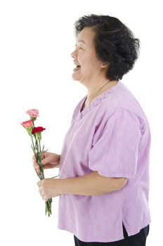Happy mothers day concept. Profile view of 60s Asian senior adult woman hand holding carnation flower gift and smiling, isolated on white background.