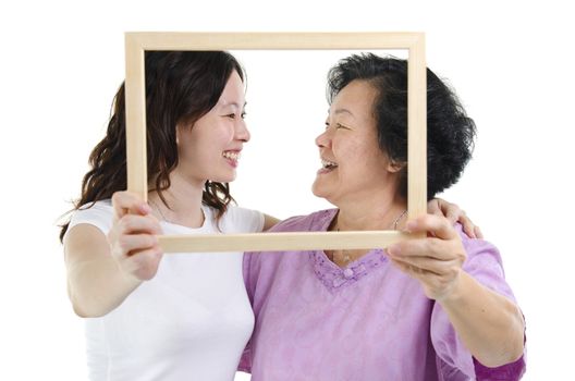 Portrait of Asian senior mother and adult daughter hands holding an empty photo frame, looking at each other, isolated on white background.