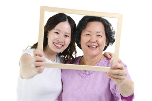 Portrait of Asian senior mother and adult daughter hands holding an empty photo frame on face, isolated on white background.