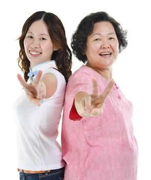 Portrait of Asian senior mother and adult daughter smiling and showing peace hand sign, isolated on white background.