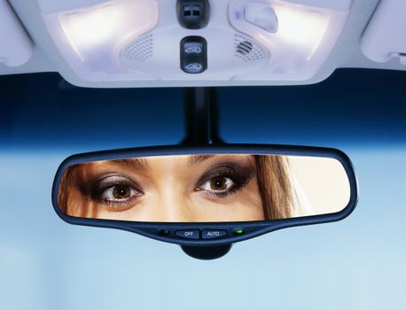 Young woman sits on driver's seat and Looks in the rear-view mirror