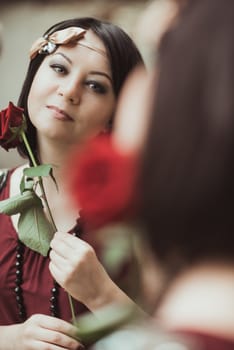 Portrait of a woman in retro style, looking in the mirror and holding a flower