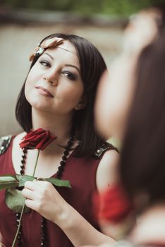 Portrait of a woman in retro style, looking in the mirror and holding a flower