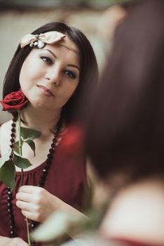 Portrait of a woman in retro style, looking in the mirror and holding a flower