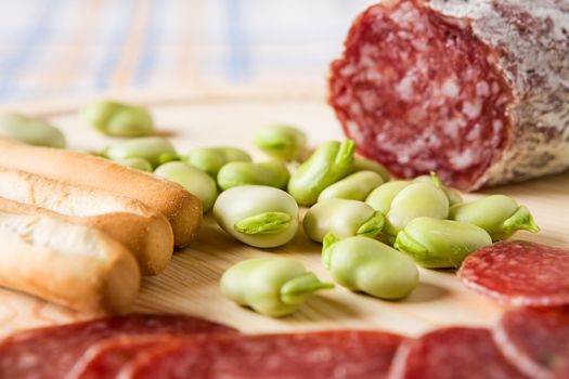 Close up of broad bean and bread sticks with Italian salami over a chopping board