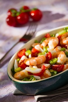 Salad of shrimps inside an oval bowl over a grey napkin