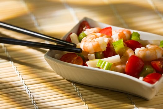 Shrimp salad inside a white bowl and chopsticks over a bamboo tablecloth