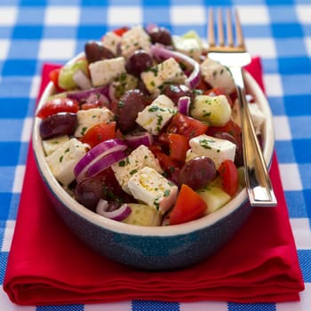 Greek salad with feta cheese olives tomatoes cucumber and onions inside an oval bowl over a red napkin