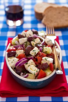 Greek salad with feta cheese olives tomatoes cucumber and onions with red wine and bread over a red napkin