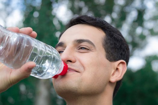 Young fitness man drinks water during training workout outdoor