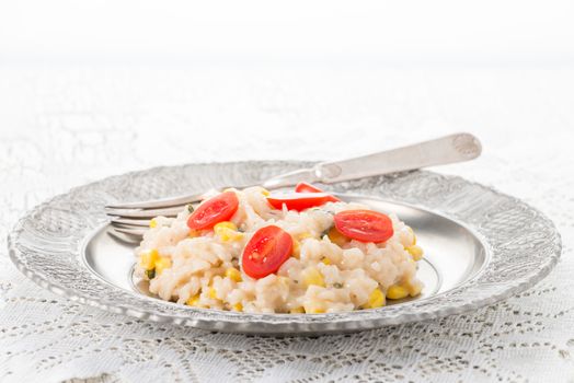 Creamy corn, basil and tomato risotto on a silver plate.