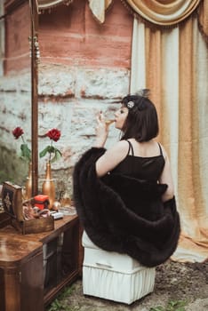 retro girl sitting at a dressing table and drinking alcohol from a glass