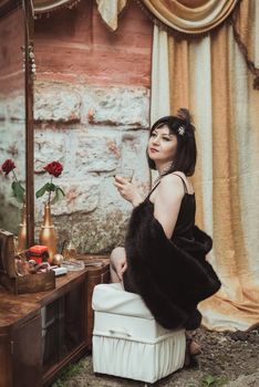 retro girl sitting at a dressing table and holding a glass of alcohol in hand