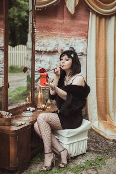 retro girl sitting at a dressing table, holding a candle and smoking cigarette with mouthpiece