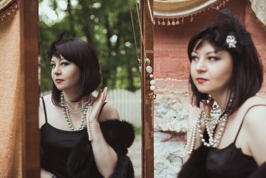 Portrait of a woman in retro style, looking in the mirror and holding a necklace