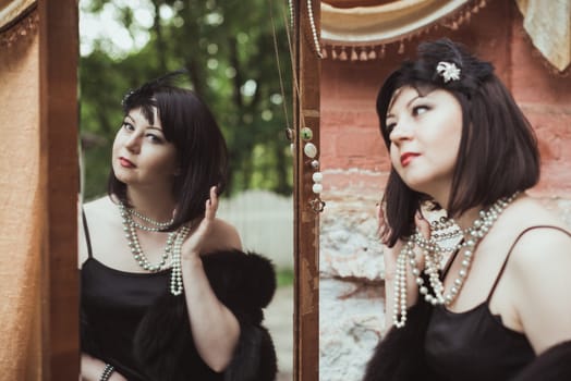 Portrait of a woman in retro style, looking in the mirror and holding a flower