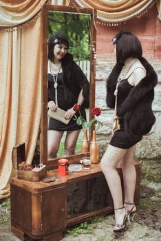 woman in retro style standing and looking in a mirror and holding small handbag