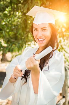 Attractive Mixed Race Girl Celebrating Her Graduation Outside In Cap and Gown with Diploma in Hand.