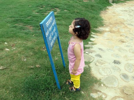 Two year old girl reading a sign board outdoors, garden, park.