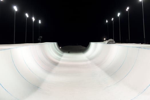 Snowboarder in a snow halfpipe night lit up by lights