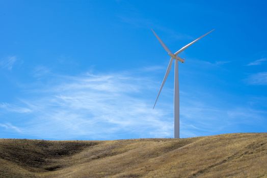 Single wind turbine on top of a hill with blue sky