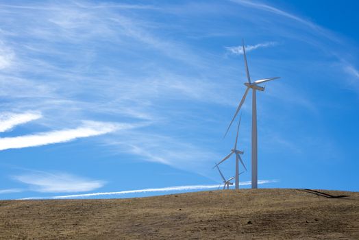 three wind turbines on top of a hill with blue sky