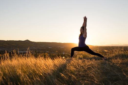 Woman doing yoga warrior I pose during evening sunset