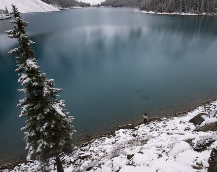 Girl skipping rocks on the shore of a blue lake in the snow