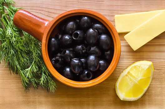 Black olives in a Cup, cheese, a slice of lemon and dill on wooden table