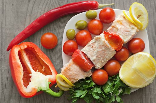 Salmon skewers on a plate with vegetables and greens. Wooden background.