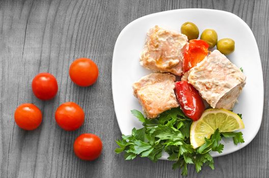 Salmon, grilled with lemon and vegetables. On a white plate and a gray wooden background.