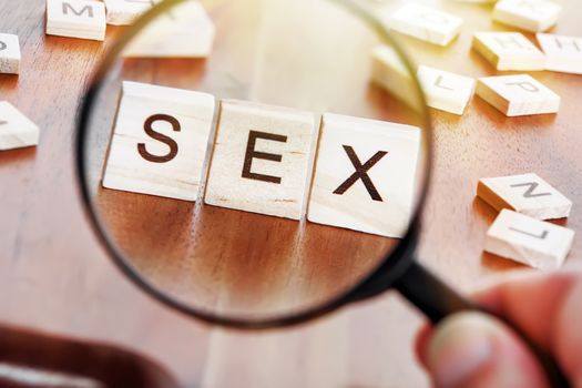 concept image of a magnifying glass zoom on a word SEX placed on a desk in precious wood