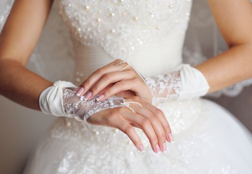 bride in white dress puts gloves on hands.