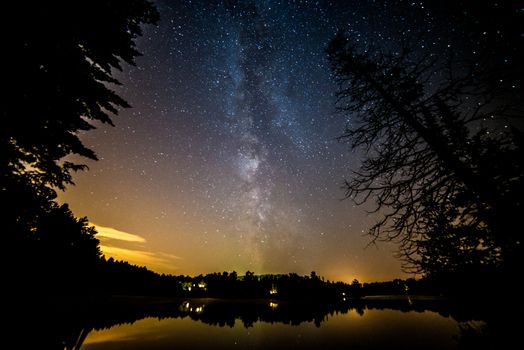 Milky way framed by trees over a lake during the summer in canada