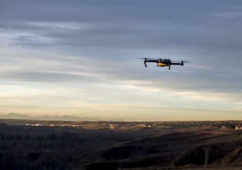 Small modern drone hovering taking picture of mountains at sunset