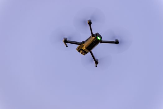 Close up of small modern drone taking photo while hovering against blue sky