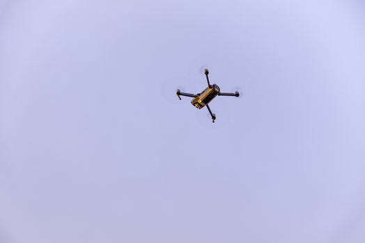 Close up of small modern drone taking photo while hovering against blue sky