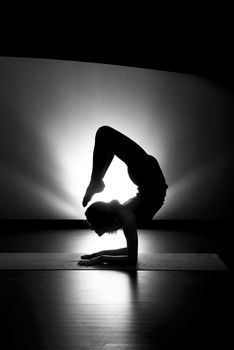 Woman doing yoga scorpion pose silhouette black and white in studio