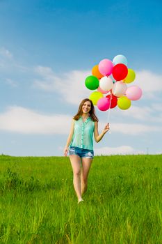 Young beautiful woman having fun with balloons on a green meadow