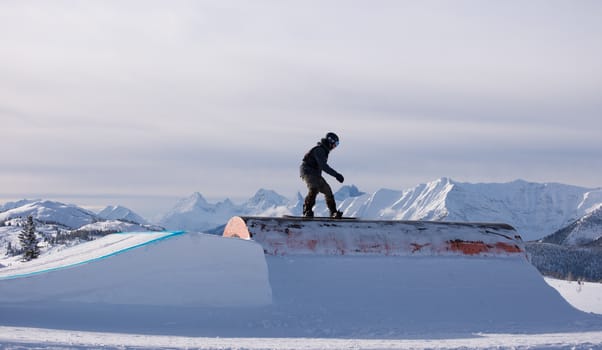 Snowboarder sliding a rail with the mountains in the background