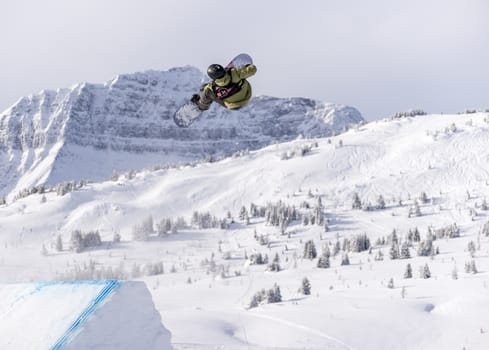 Snowboarder spinning doing a grab in the air off a jump