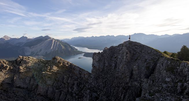 Young man looks out from the peak of a mountain overlooking lake