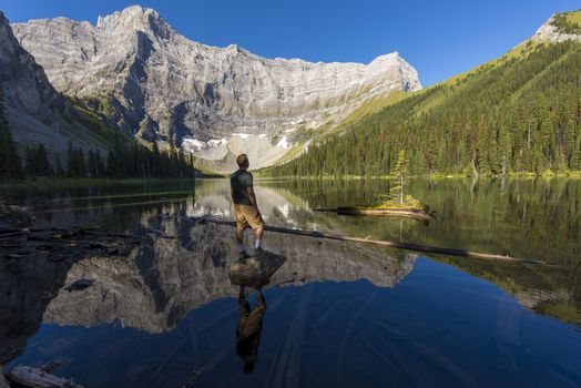 Young man standing on a rock in a lake looking up at mountains