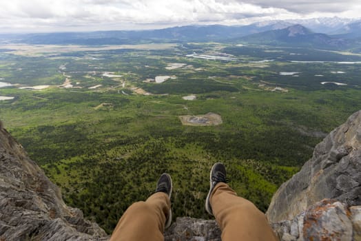 legs overhanging steep cliff wall above a beautiful landscape